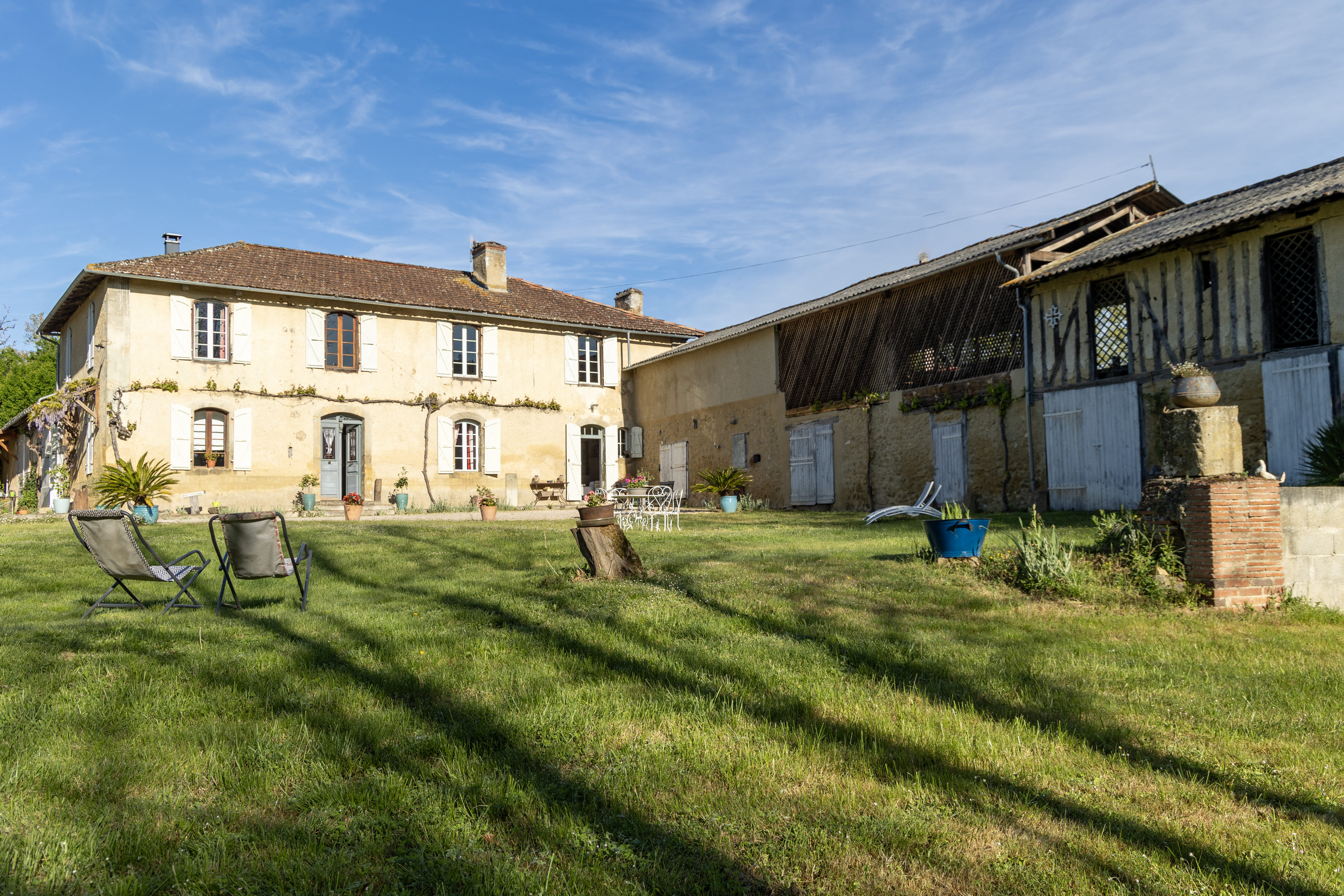 Vue extérieure du gîte avec une maison en pierre et un jardin verdoyant, équipée de chaises de jardin.